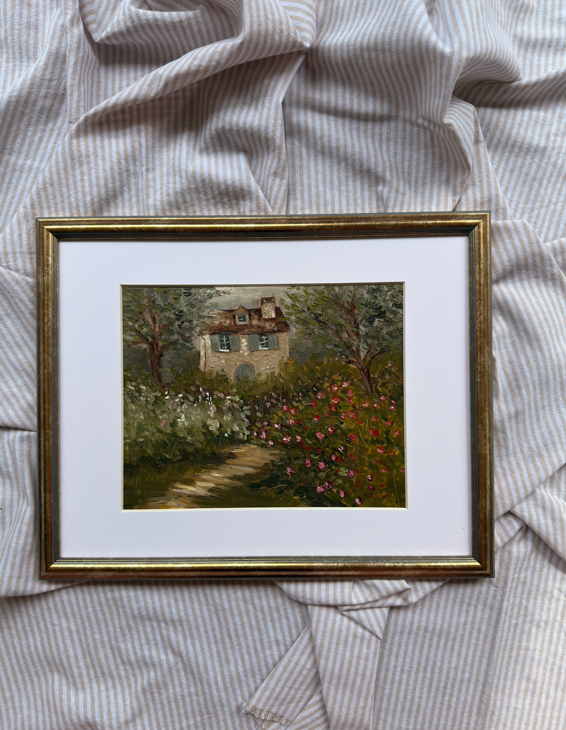 Framed painting of a house with a garden on a textured fabric background