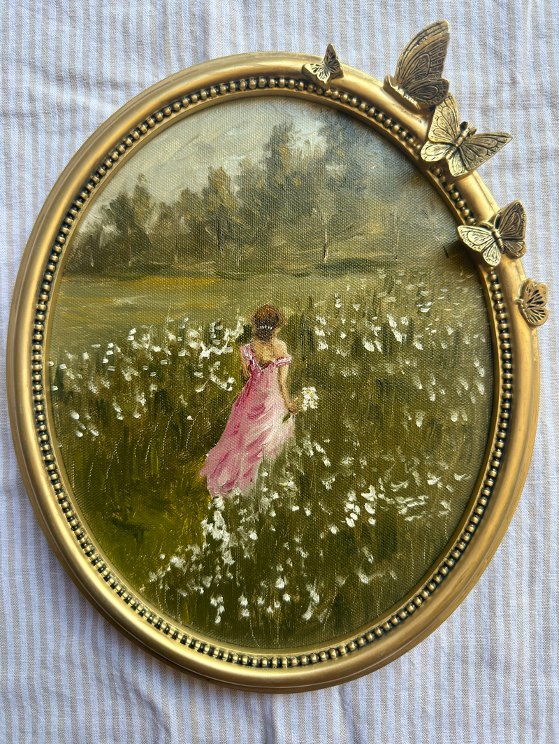 Round painting of a woman in a pink dress standing in a field with butterflies on a textured fabric background.